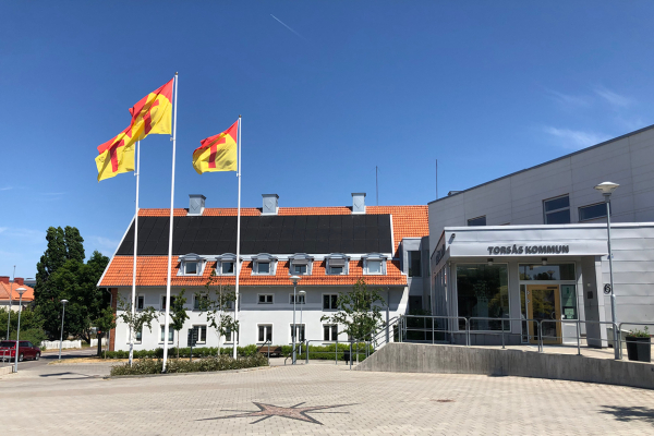 Torsås kommunhus en solig sommardag med blå himmel med Torsåsflaggorna som vajar i vinden.
